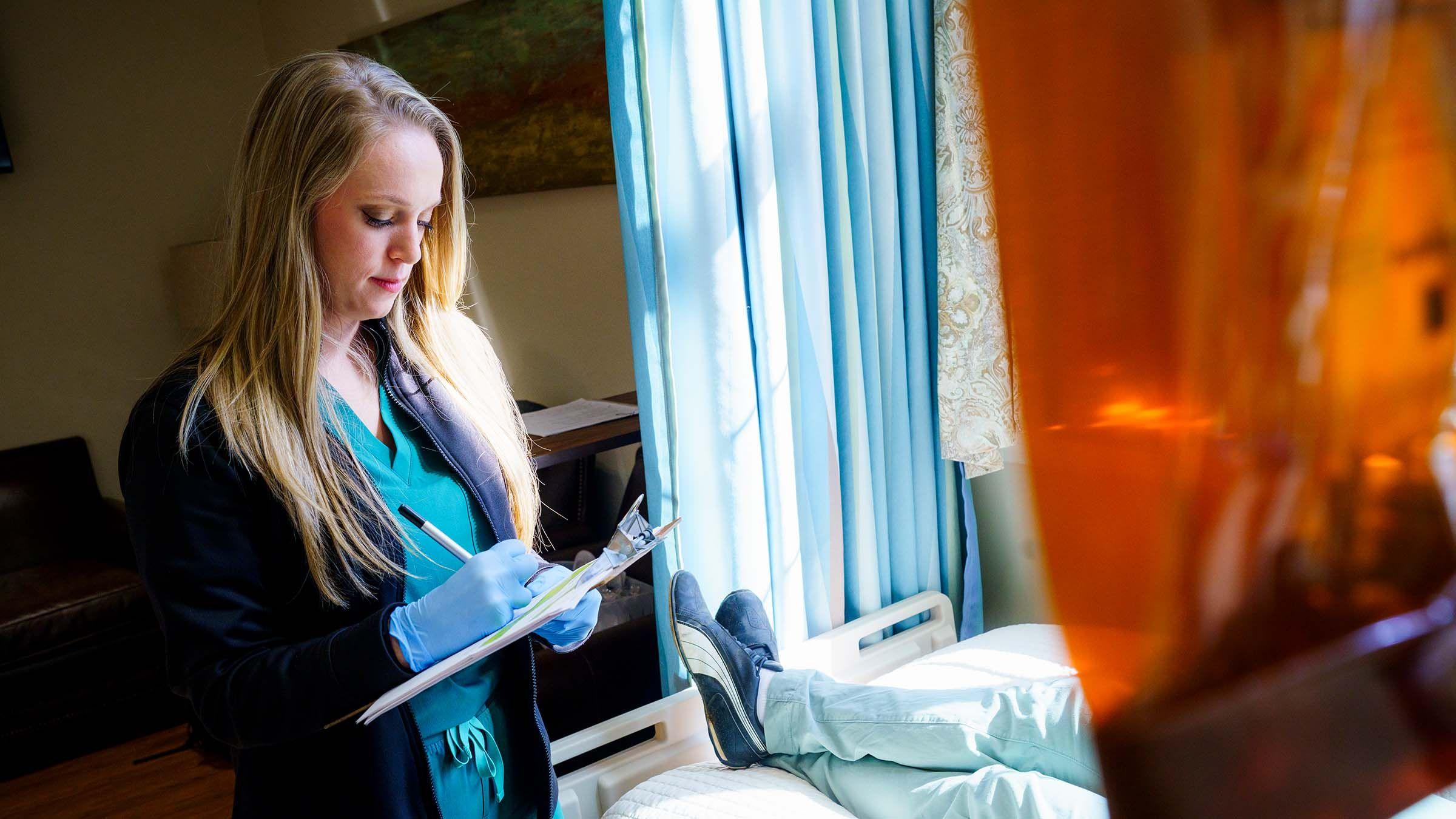 Pinnacle nurse writing on a clipboard at a participant's bedside